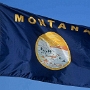 Flagge Montanas<br />Das Band im unteren Teil enthält den spanischen Schriftzug „Oro y plata“ (deutsch Gold und Silber), ein Verweis auf die Geschichte der Gold- und Silberfunde. Das Band ragt bis auf den äußeren Ring. Der äußere Ring enthält den Schriftzug das große Siegel des Staates Montana und ein Kreuz am untersten Punkt.<br /><br />1846 überließ Großbritannien im Zuge des Oregon-Kompromisses den USA auch den Nordwesten Montanas, das allerdings 1861-1864 Teil des Dakota-Territoriums wurde. 1862 begann der Goldrausch am Grasshopper Creek und später in Virginia City, und lockte tausende in das dünn besiedelte Gebiet. Bereits 1864 wurde Montana zu einem eigenständigen Territorium, Virginia City bis 1875 die Hauptstadt.<br />Zwischen 1864 und 1889 wurde Montana als Territorium organisiert. Es entstand aus der Umbildung des größeren Idaho-Territoriums. Im ersten Jahr als Territorium war Bannack die Hauptstadt. Es wurde jedoch schon 1865 von Virginia City als Capitol City abgelöst. 1875 wurde die Hauptstadt nach Helena verlegt. Die Aufnahme als Bundesstaat in die USA erfolgte 1889 - Montana wurde somit 41. Bundesstaat