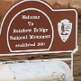 Die Rainbow Bridge befindet sich in einem Seitencanyon des Lake Powell in Utah, ca. 13 km nördlich der Grenze zu Arizona. Sie ist die größte natürliche Steinbrücke der Welt mit einer Spannweite von 82 m und einer Höhe von 88 m. Ihr Bogen ist an seiner höchsten Stelle 10 m breit und 12 m dick. Die Rainbow Bridge wurde 1910 von Präsident William Taft zum National Monument erklärt.<br /><br />Der Brückenbogen besteht im oberen Teil aus Navajo-Sandstein und am Fuß aus Kayenta-Sandstein. Er entstand, als das Wasser des Flusses die dünne Wand zur anderen Seite eines Mäanders durchbrach und im Laufe der Zeit die riesige Öffnung formte.<br /><br />Die Rainbow Bridge ist ein Heiligtum der Navajo-Indianer, die sie Nonnezoshi (Navajo: "versteinerter Regenbogen") nennen. Nach einer Legende retteten sich einige Navajo vor einer Sintflut durch die Brücke, die die einzige Öffnung zwischen der einstigen Vorwelt und der Welt von heute darstellt. Deshalb ist es seit 1995 verboten, unter der Rainbow Bridge hindurchzugehen oder sie gar zu erklettern.<br /><br />Besucht am 31.5.2014, überflogen am 2.10.2015