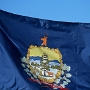 Die aktuelle Flagge des US-Bundesstaats Vermont wurde im Jahr 1923 eingeführt. Sie zeigt auf blauem Untergrund das Staatssiegel. Die blaue Farbe basiert auf der früheren Bürgerwehrflagge. Das Siegel mit der einzelnen Kiefer geht zurück auf ein Siegel aus der Zeit von 1777 bis 1791, als Vermont für einige Jahre unabhängig war. Das aktuelle Siegel stammt aus dem Jahr 1821 und symbolisiert den „Green Mountain State“, den „Grünen Bergstaat“.<br /><br />Auf einem Spruchband steht der Name Vermont und das Motto des Staates:<br />„Freedom and Unity“„Freiheit und Einigkeit“